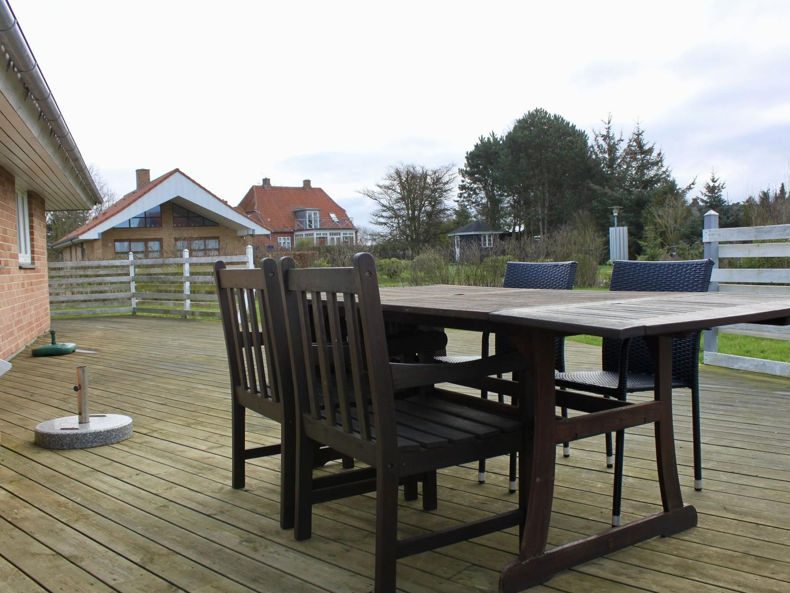Holzterrasse mit Tisch und Stühlen. Blick auf Garten und Nachbarhäuser.