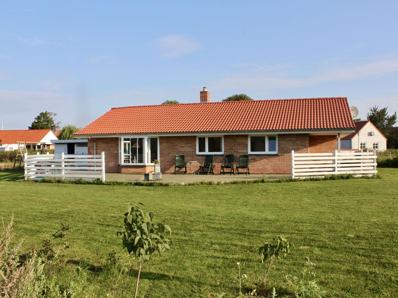 Ein Haus mit rotem Dach und weißer Umzäunung auf einer grünen Wiese.
