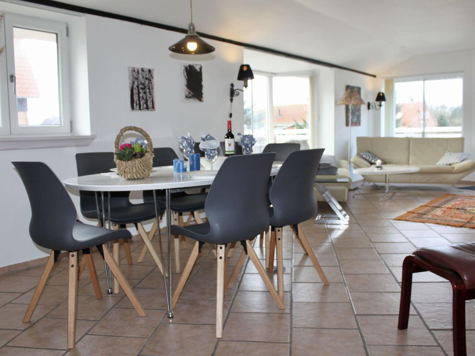 Essbereich mit Tisch und Stühlen, Wohnbereich mit Sofa und Fenstern.