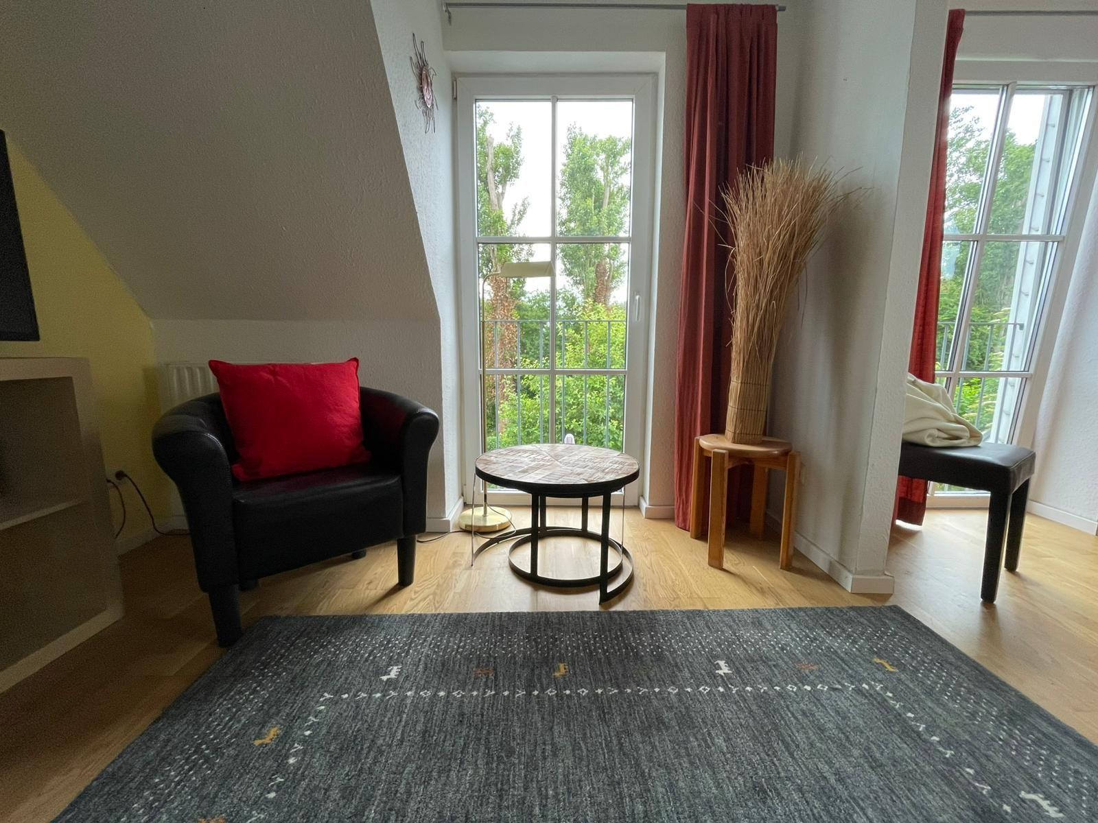 Schlafzimmer mit Sitzgelegenheit und Balkonblick. Holzboden und Teppichboden.