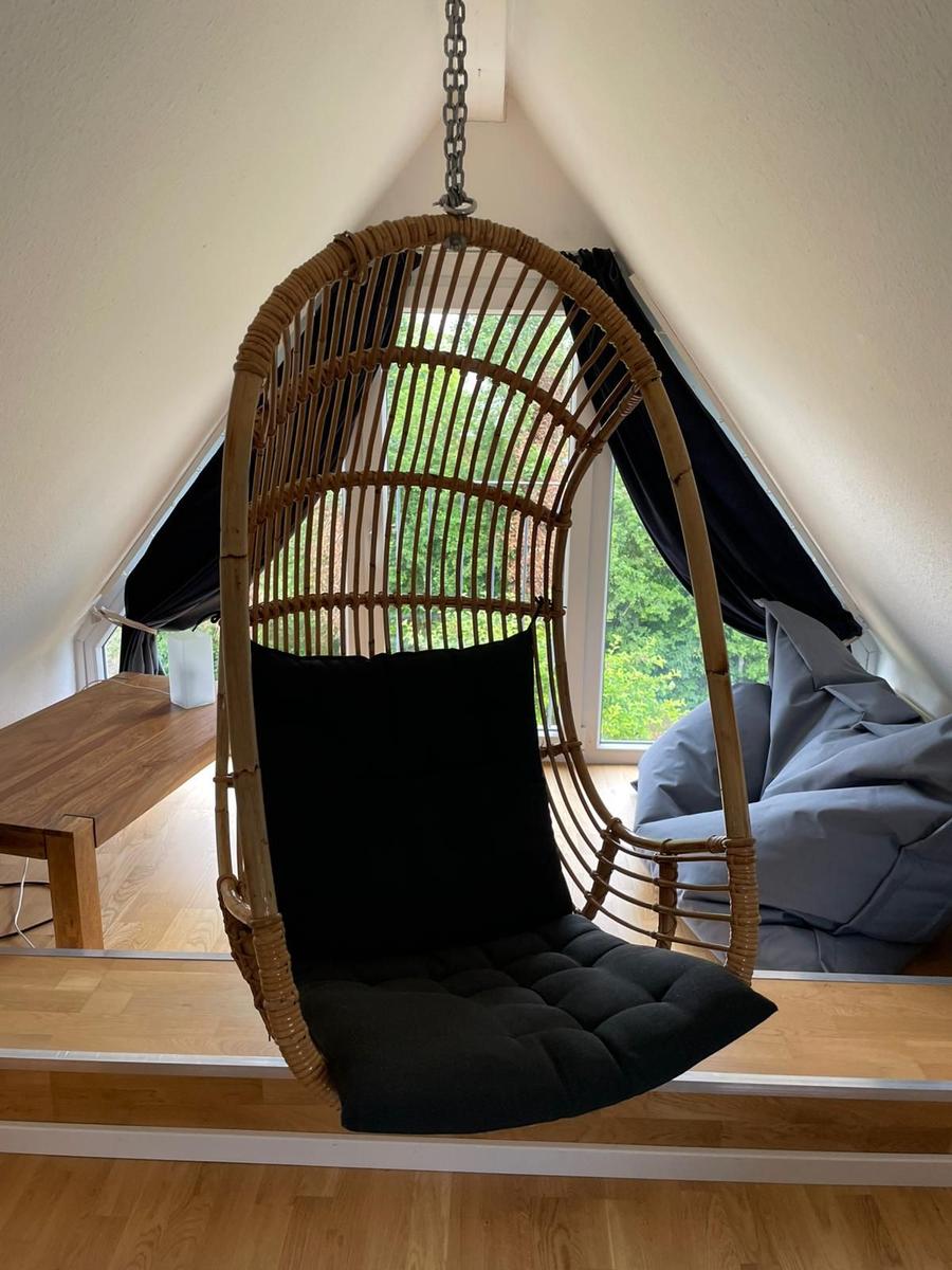 Hängesessel aus Rattan mit schwarzer Polsterung im Dachbodenraum mit Fenster.