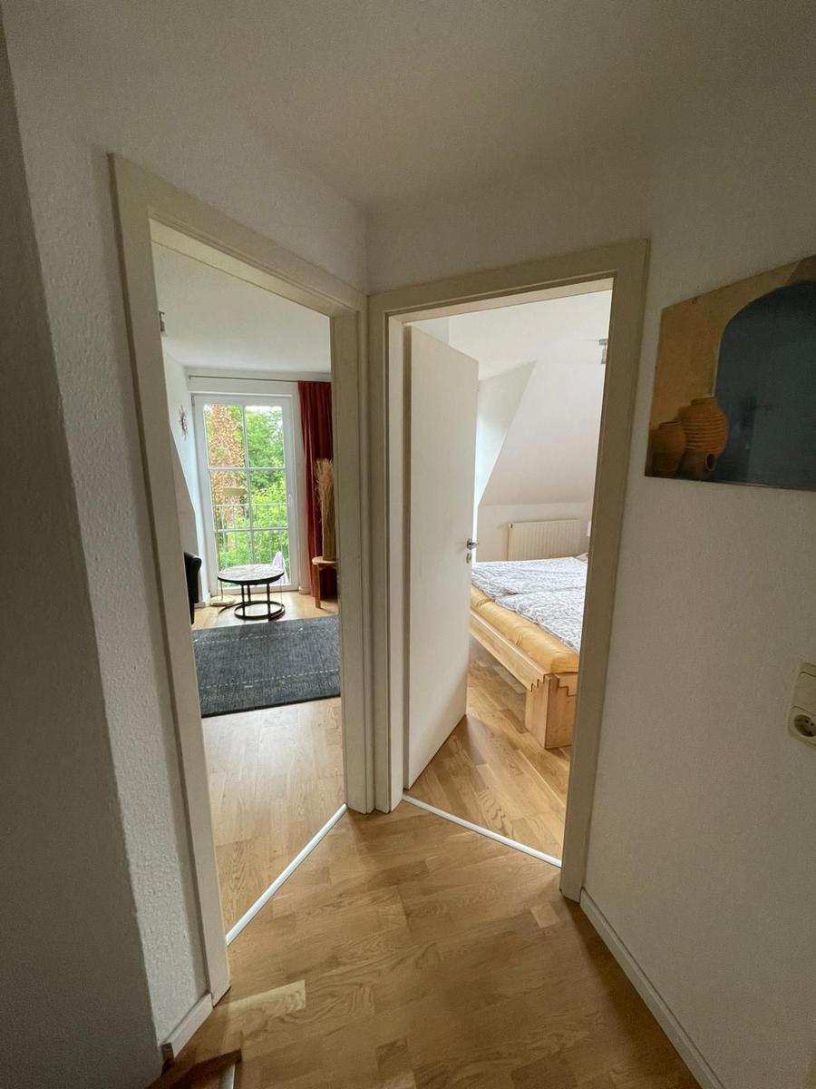 Hinter dem Flur sind Schlafzimmer und Wohnbereich mit Fenster und Holzboden sichtbar.