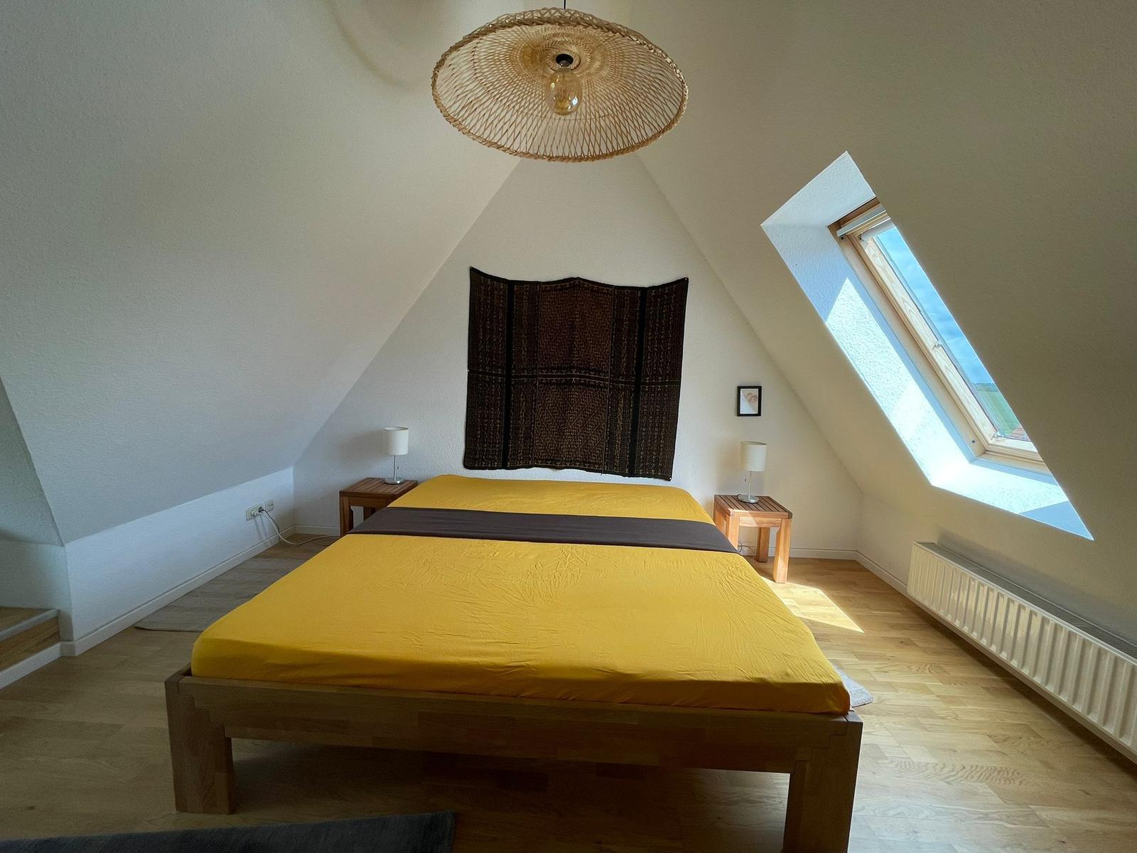 Schlafzimmer mit Dachschräge, gelbem Bett und Dachfenster.