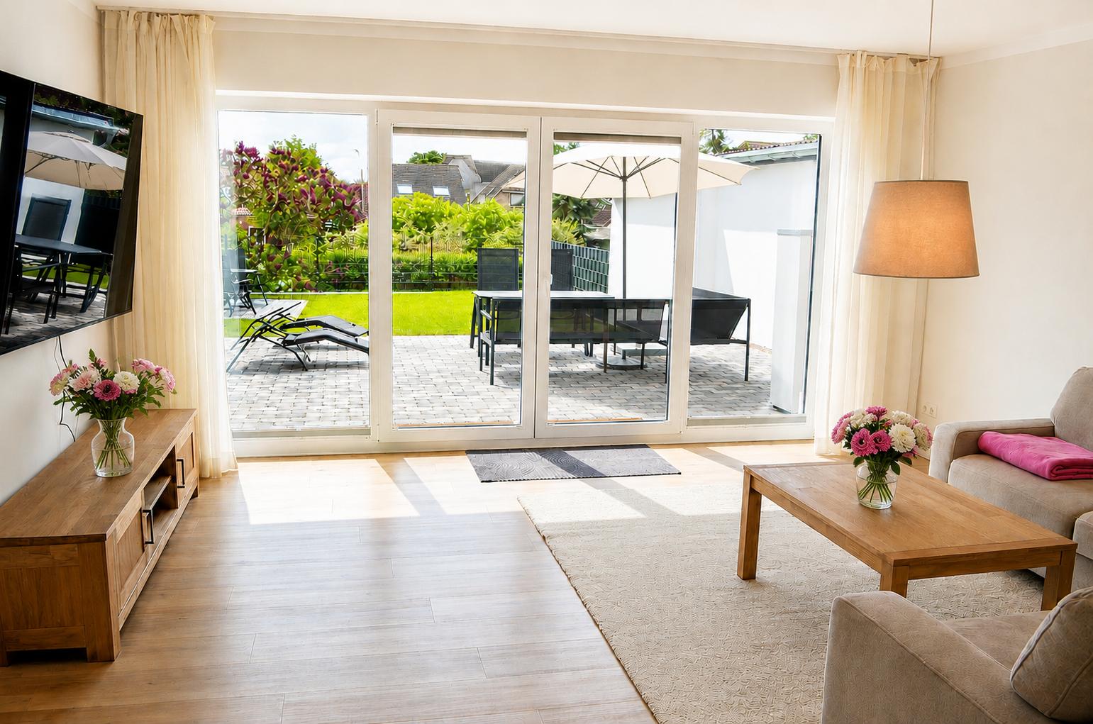 Wohnzimmer mit Terrasse, Sofa, Couchtisch und TV. Draußen Liegen und Tisch.