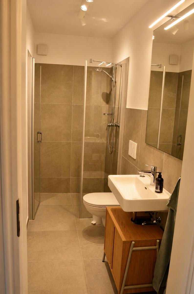 Badezimmer mit Dusche, WC und Waschbecken auf Holzschrank