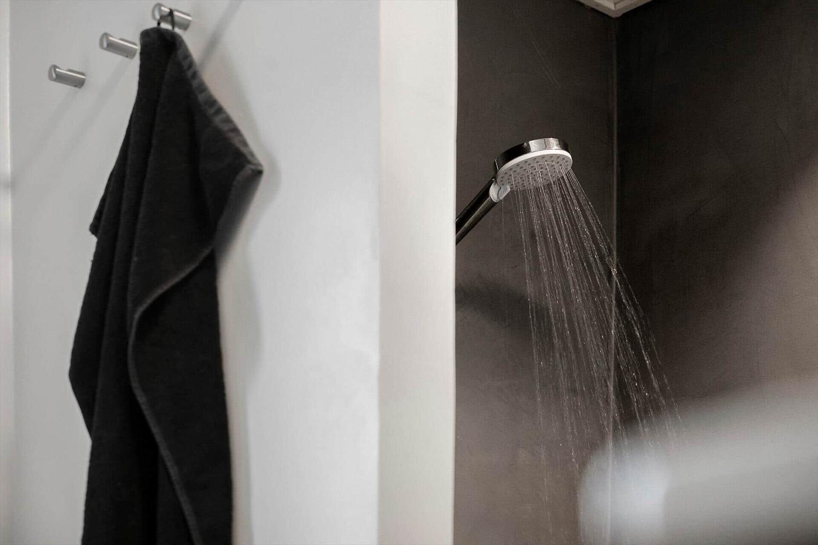Duschkopf mit laufendem Wasser. Schwarzes Handtuch hängt an Wandhalterungen.