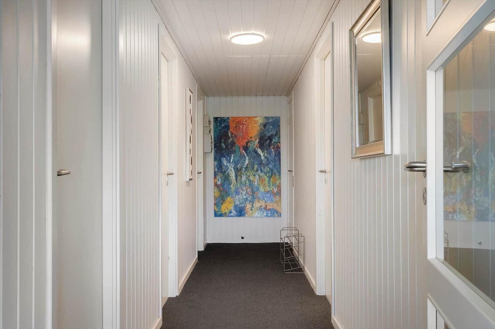 Flur mit weißen Wänden, dunklem Teppich und abstraktem Wandbild.