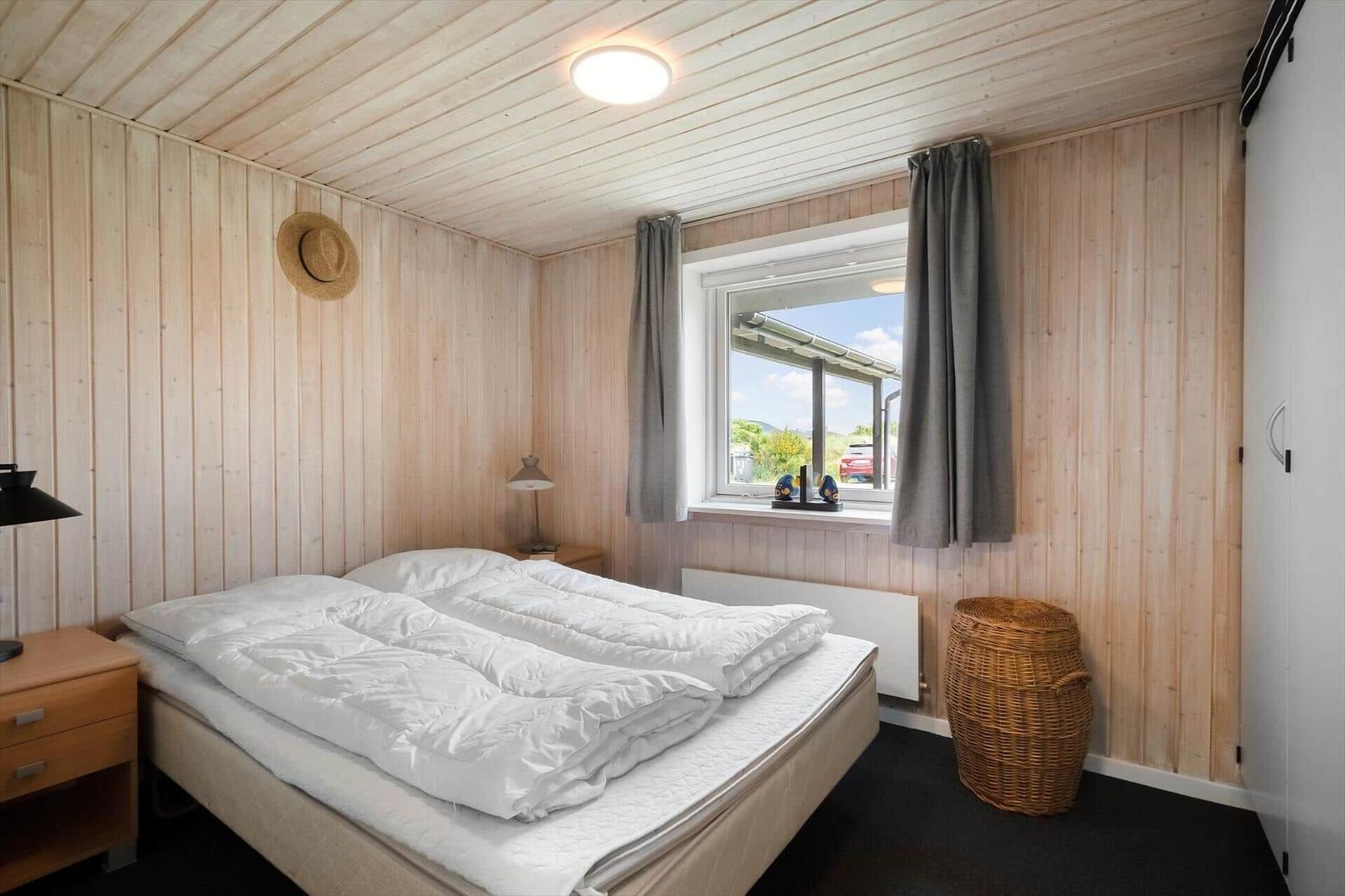 Schlafzimmer mit Bett, Fenster, Vorhängen und Korb.