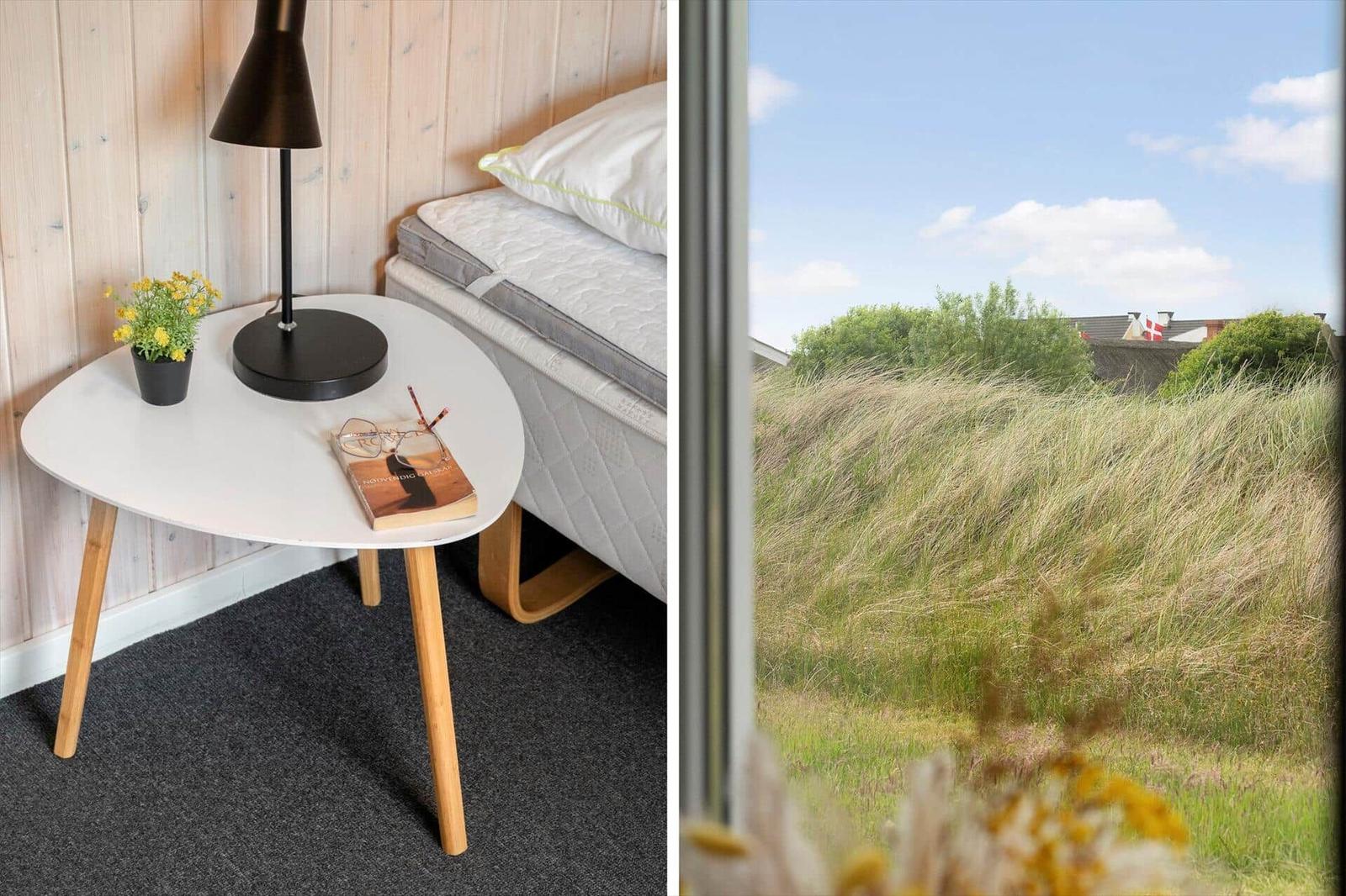Schlafzimmer mit Bett, Tisch und Lampe. Aussicht auf Gras und Himmel.