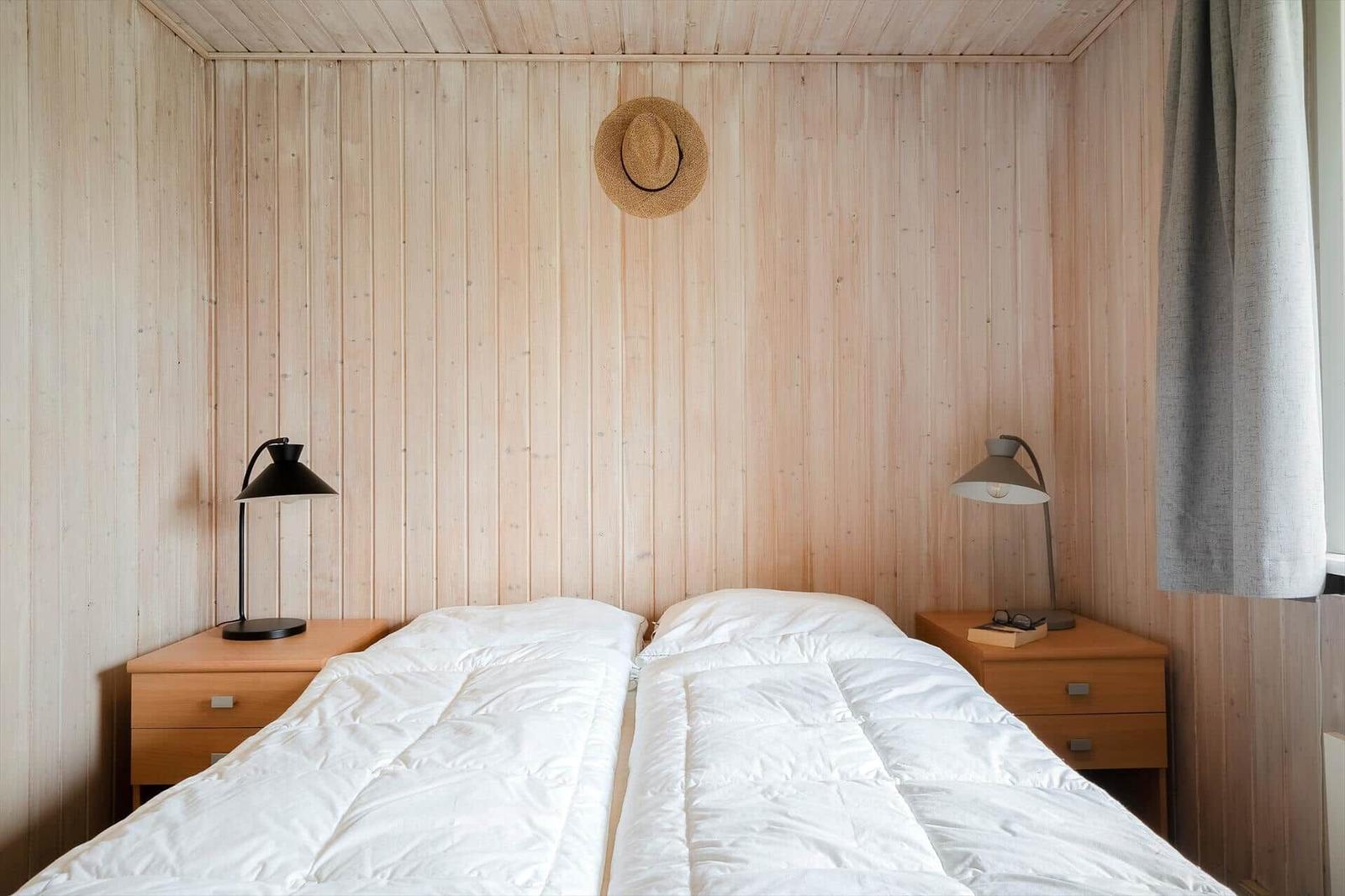 Zimmer mit zwei Betten, Holzwänden und Nachttischen mit Lampen.