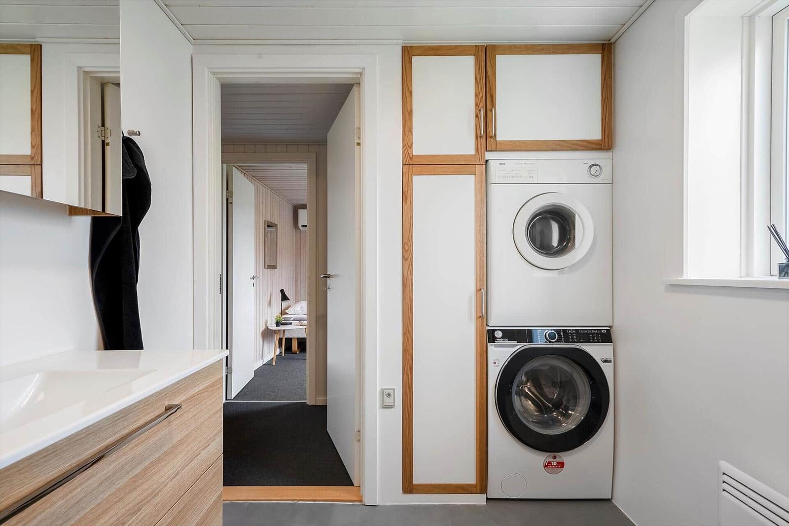 Wäscherei mit Waschmaschine und Trockner, integriert in Holzschrankwand. Blick in Schlafzimmer.