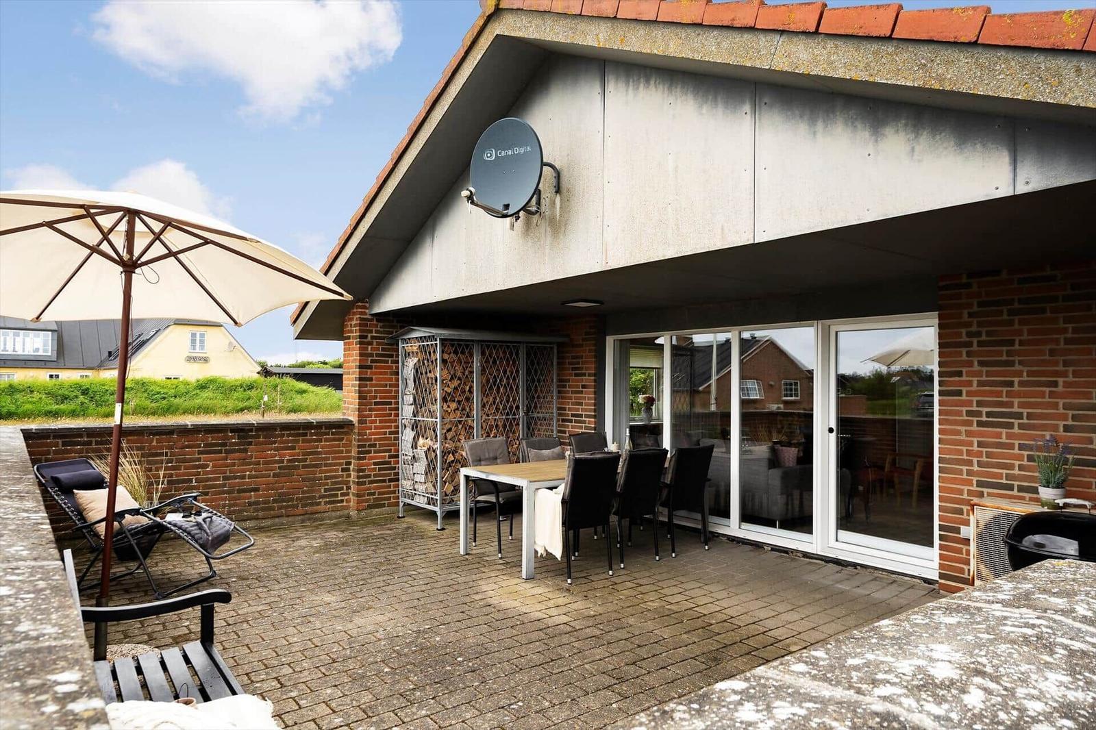 Terrasse mit Tisch, Stühlen, Sonnenschirm und Grill. Glasfront führt ins Haus.