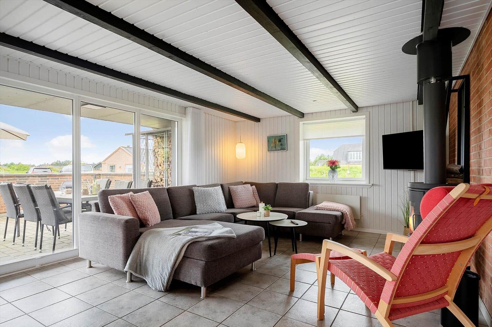 Wohnzimmer mit Sofa, roter Sitzgelegenheit und Kamin. Große Glasfront zum Balkon.