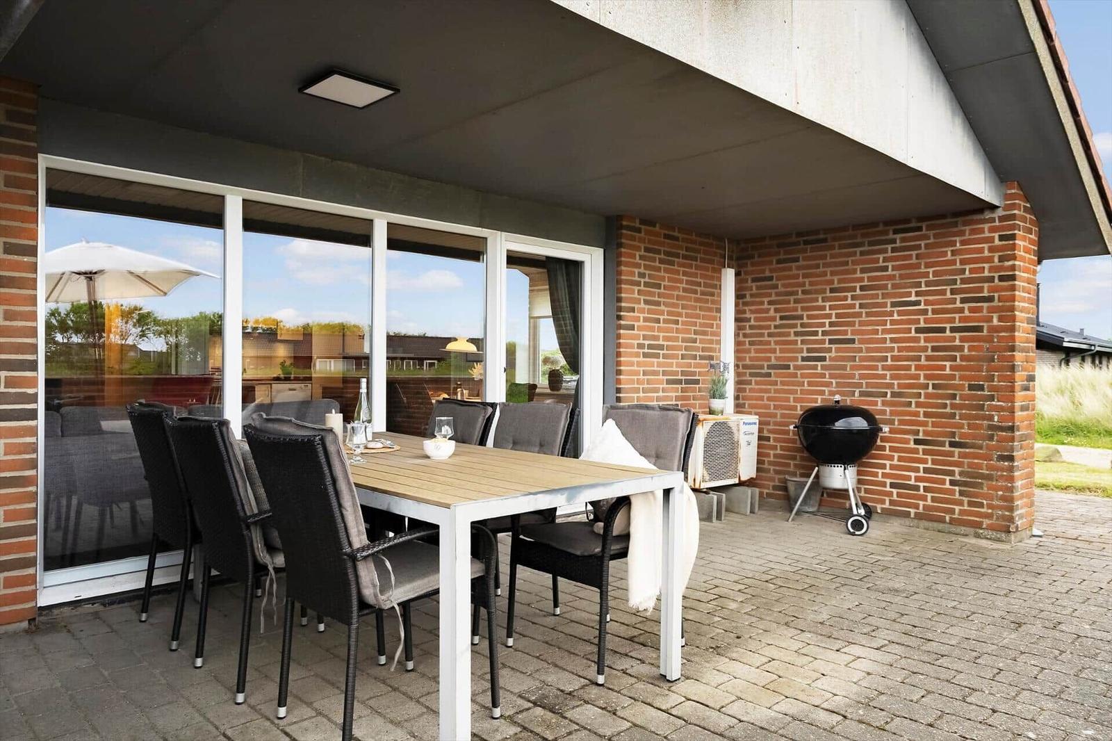 Terrasse mit Esstisch, Stühlen und Grill. Große Fensterfront. Ziegelmauer und Pflasterung.