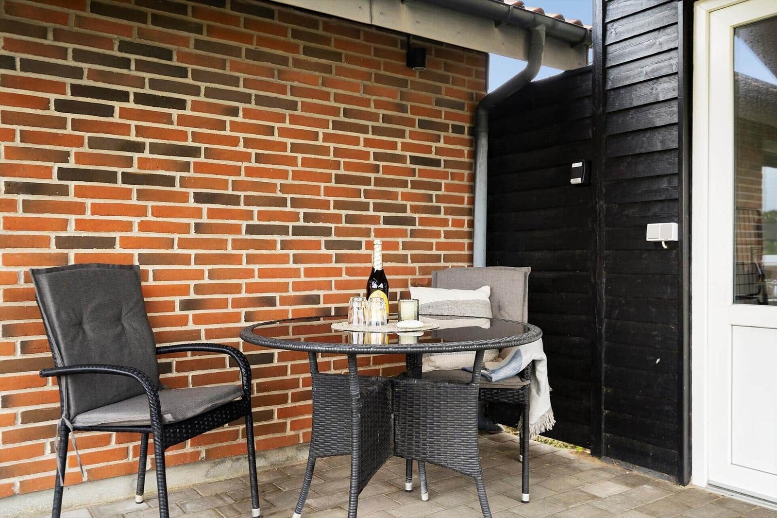 Terrasse mit Tisch und zwei Stühlen vor roter Ziegelwand.