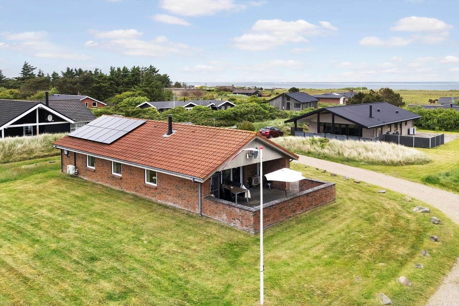 Ein Haus mit rotem Dach und Solarpanelen auf einer grünen Wiese mit Blick aufs Meer.