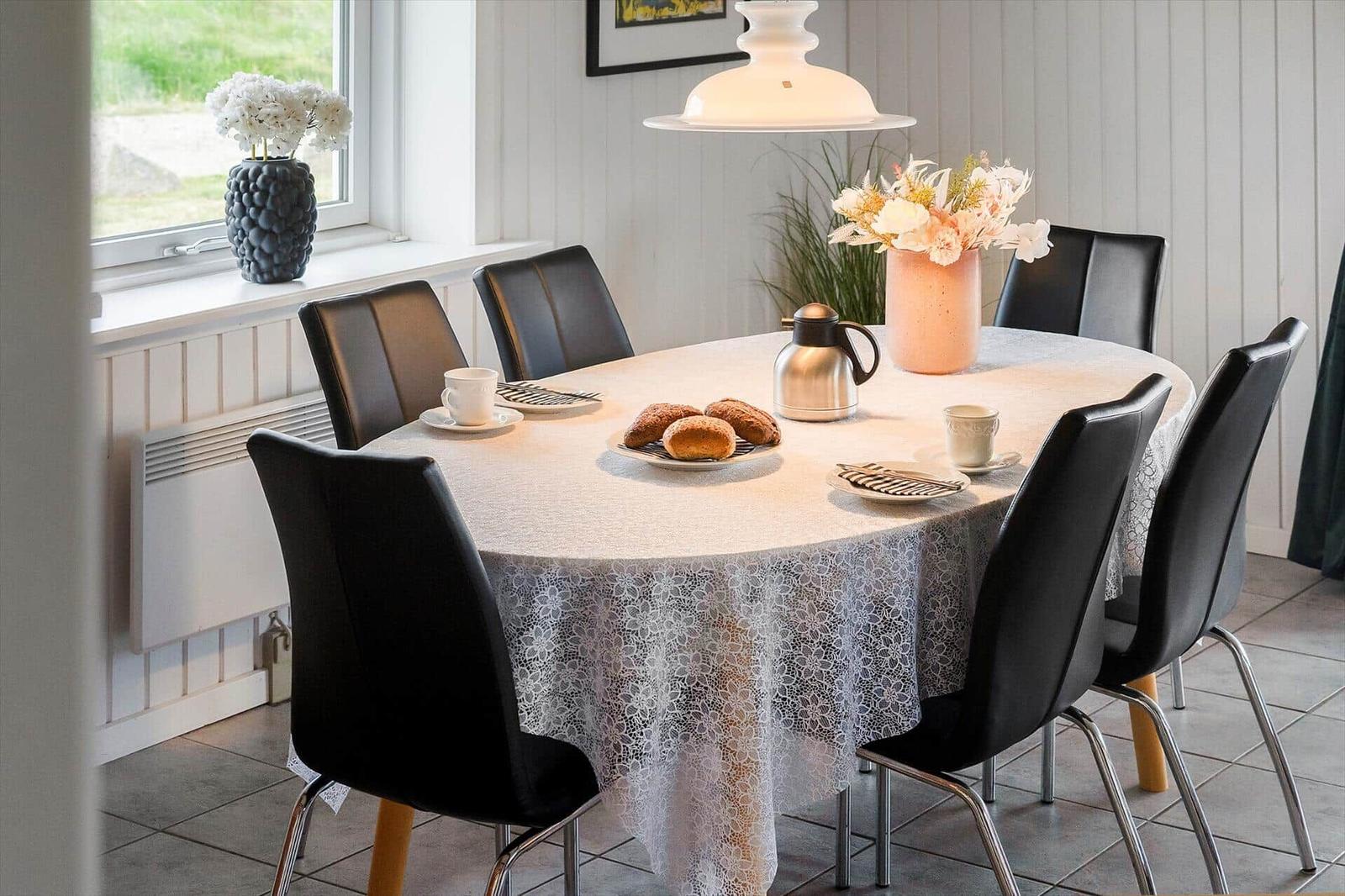 Runde Tafel mit Tischdecke, Stühle, Kaffeetasse und Brötchen.