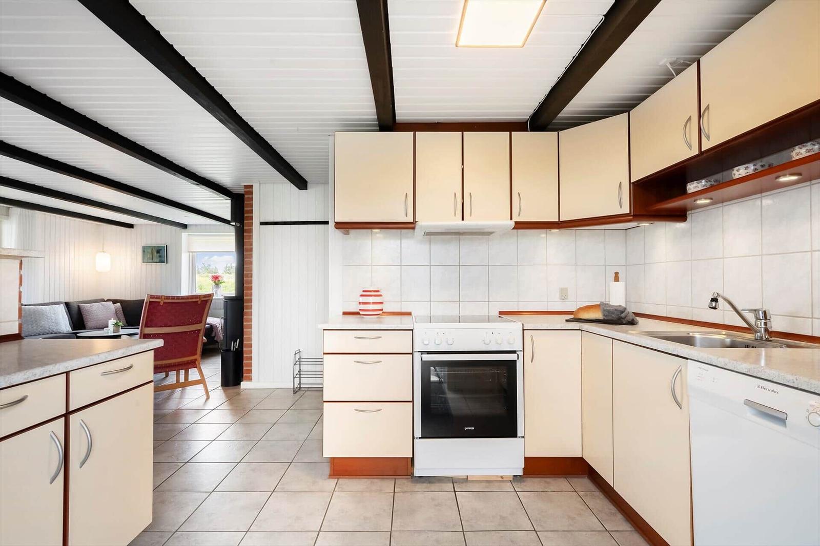 Küche mit Arbeitsplatte, Spüle, Herd und Waschmaschine. Blick in Wohnbereich mit Sofa und Stuhl.