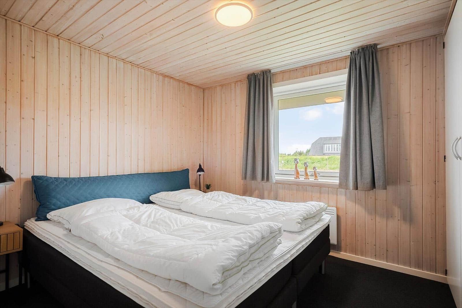 Schlafzimmer mit Holzwand und Fensterblick auf Grünfläche.