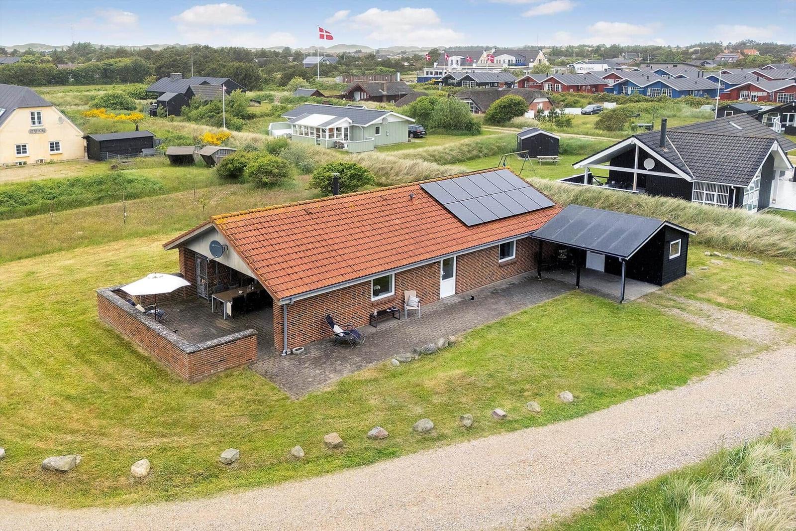 Ein Haus mit rotem Dach und Solaranlage auf grünem Grundstück mit Terrasse und Garten.