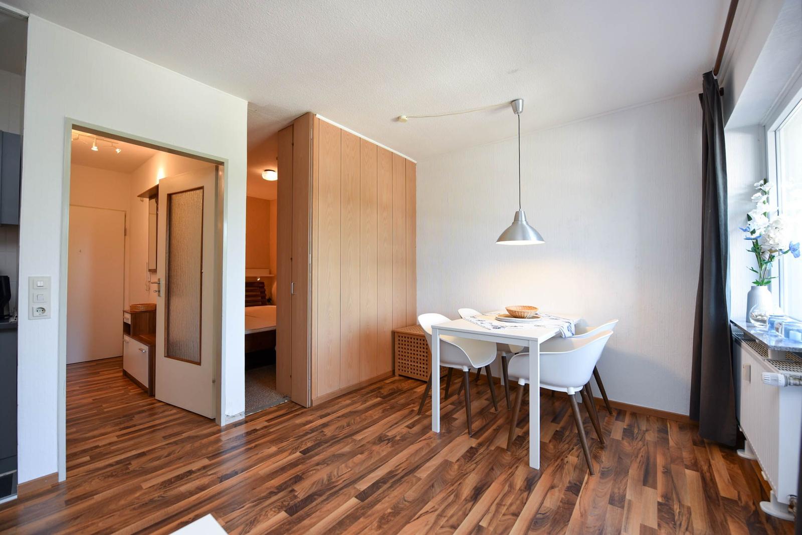 Essbereich mit weißem Tisch und Stühlen. Holzboden und Fenster mit Vorhängen.
