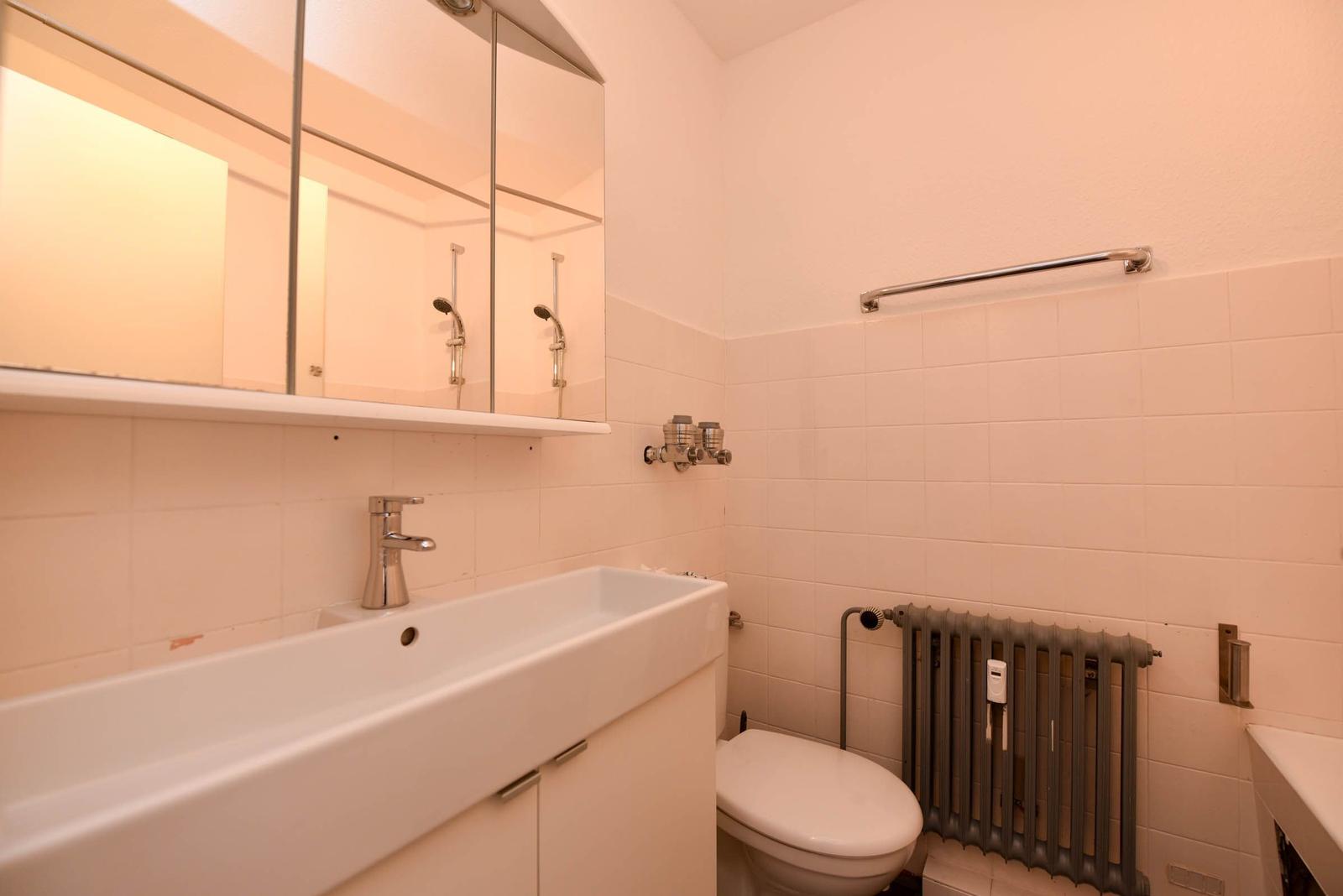Badezimmer mit Waschbecken, Spiegel, Toilette und Heizkörper.