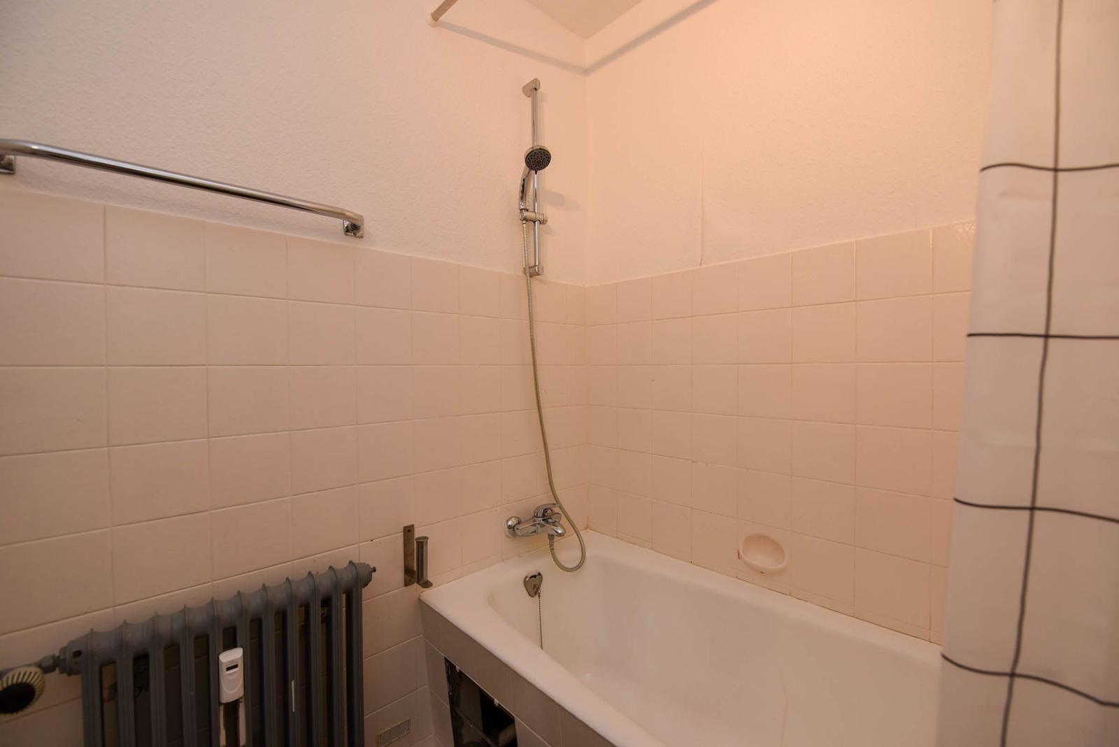 Bad mit Badewanne, Duschbrause und Heizkörper an der Wand.
