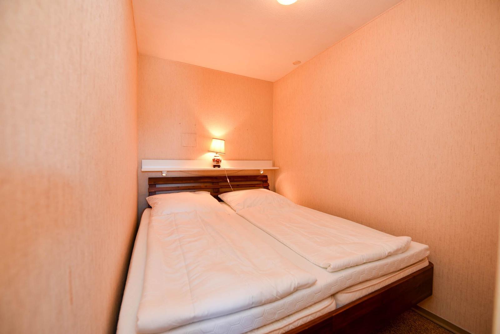 Ein Schlafzimmer mit Doppelbett, weißen Bettwäsche und einer Wandlampe.
