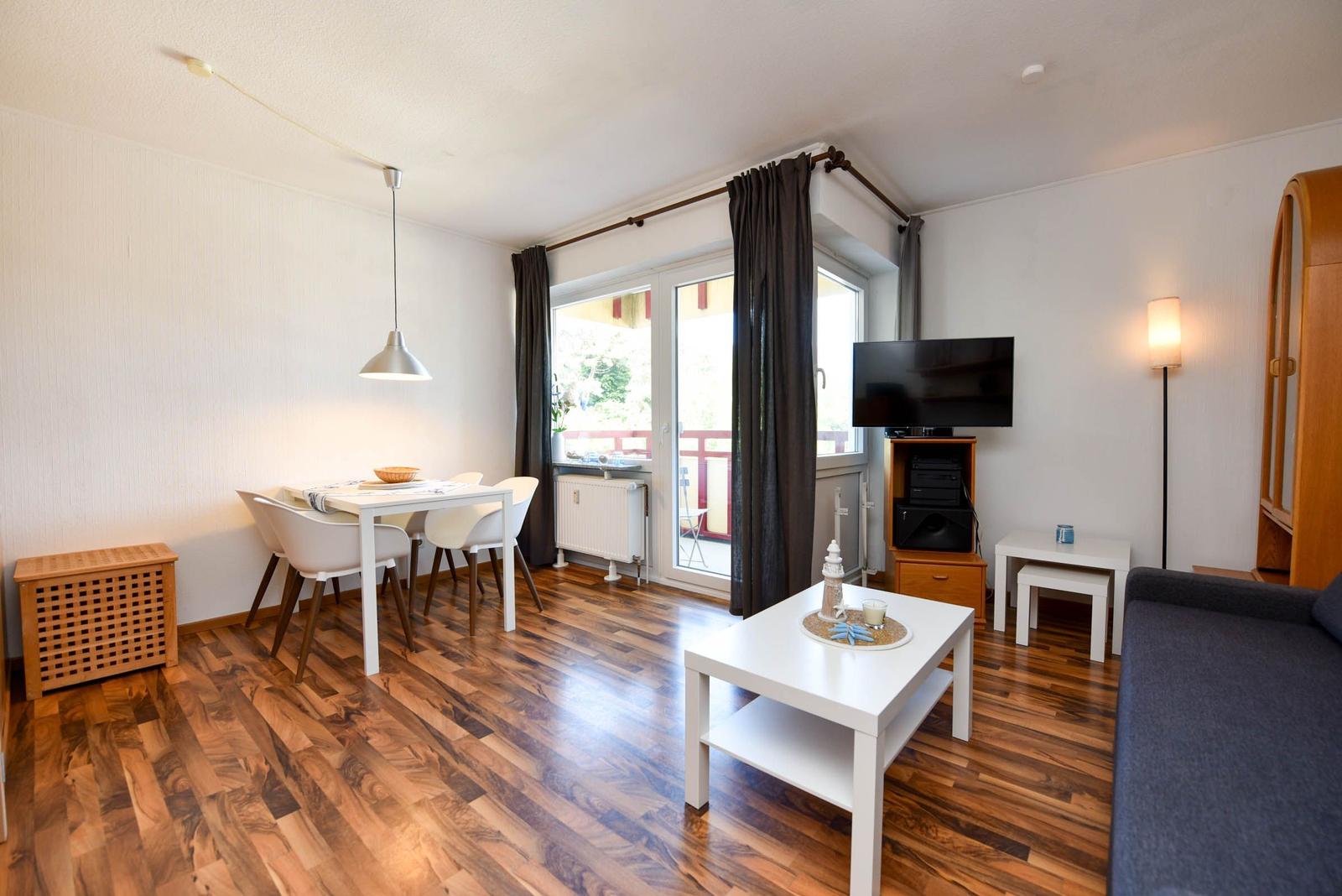 Wohnzimmer mit Essbereich, TV und Balkon. Holzboden und weiße Möbel.