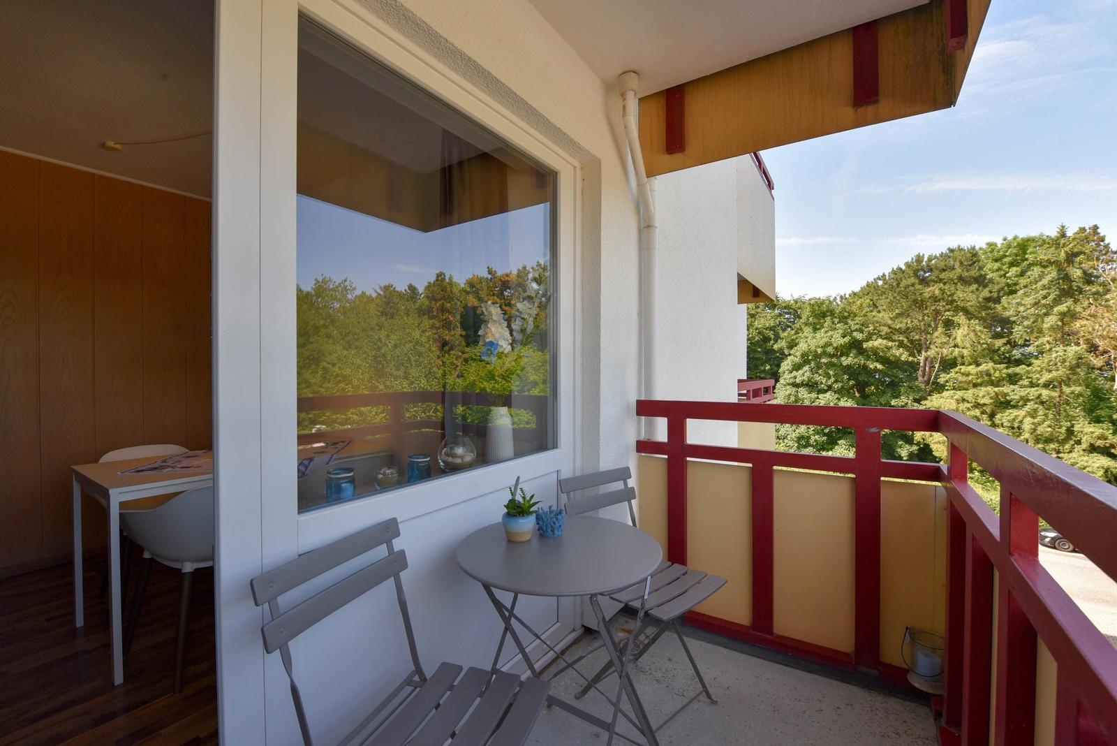 Balkon mit Tisch und Stühlen, rote Brüstung, Blick auf Bäume.