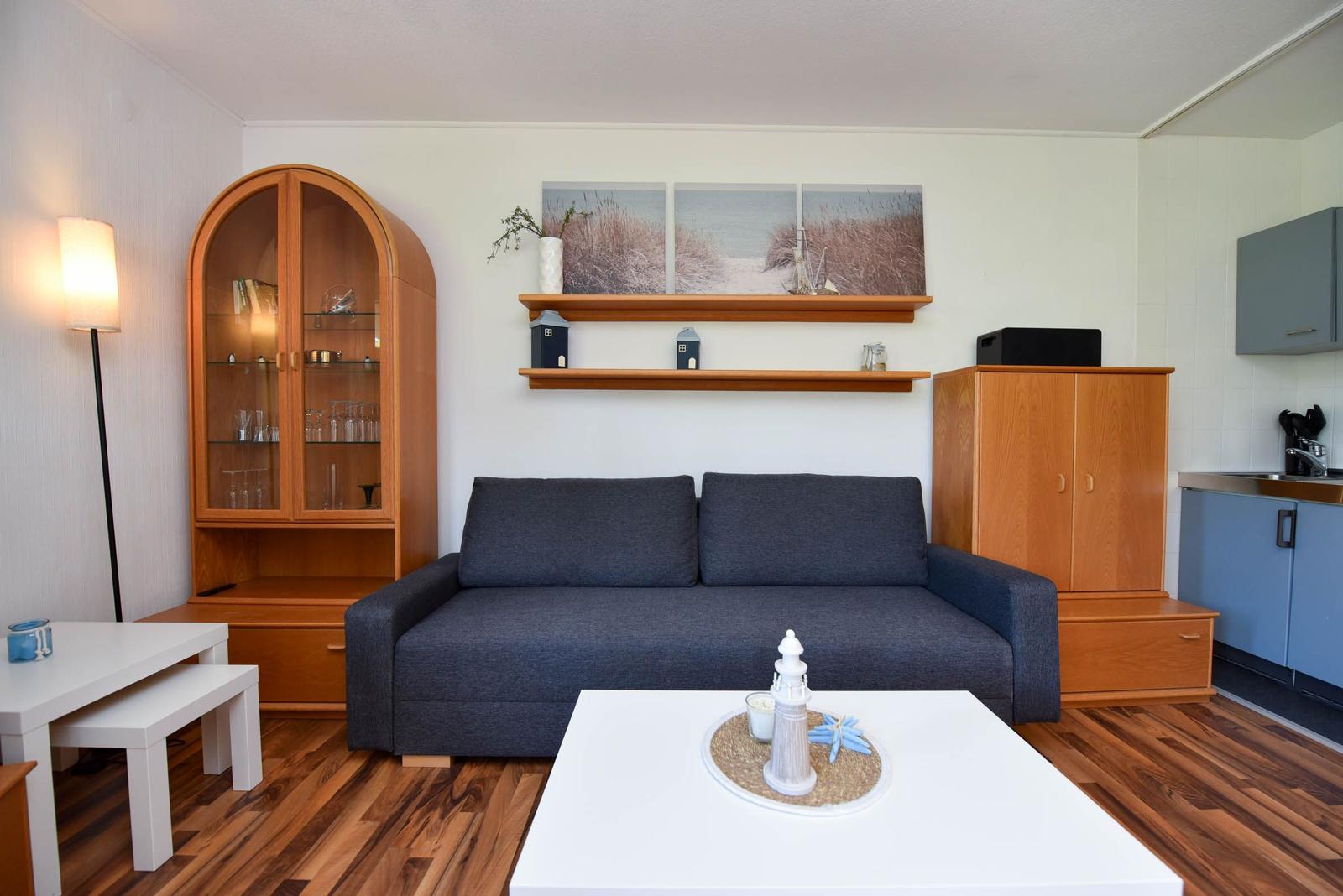 Wohnzimmer mit Sofa, Tisch und Holzmöbel. Wandbild und Küchenbereich sichtbar.