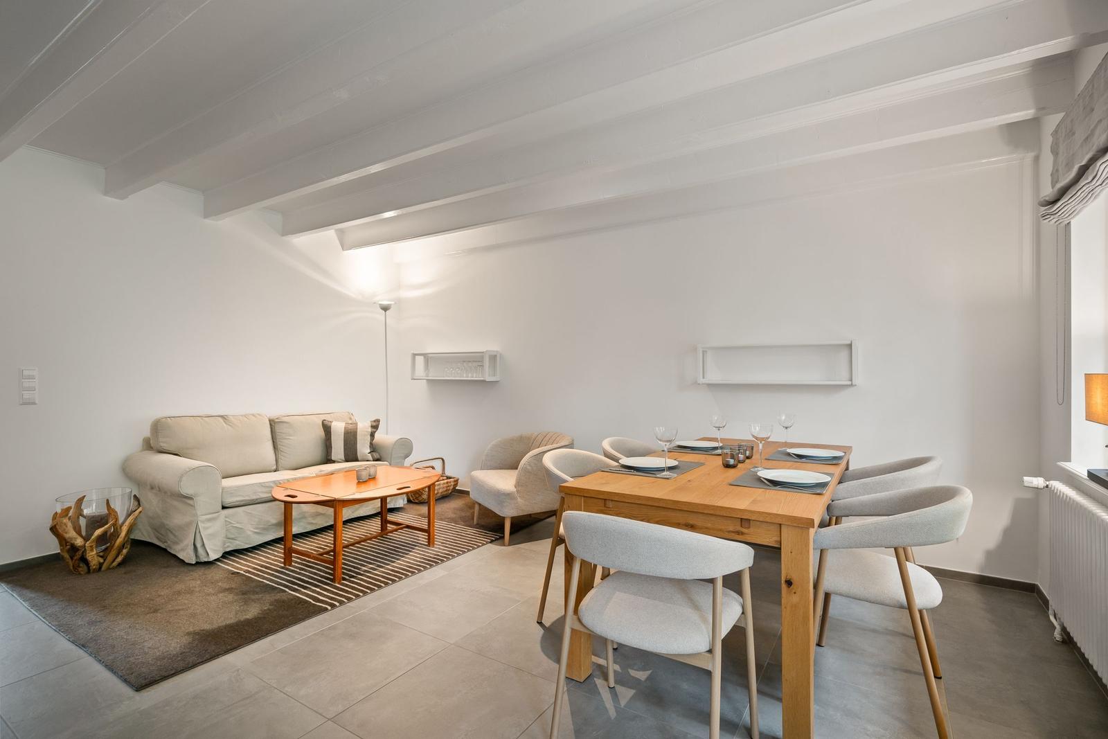 Wohn- und Essbereich mit Sofa, Tisch und Stühlen. Holzdecke und weiße Wände.