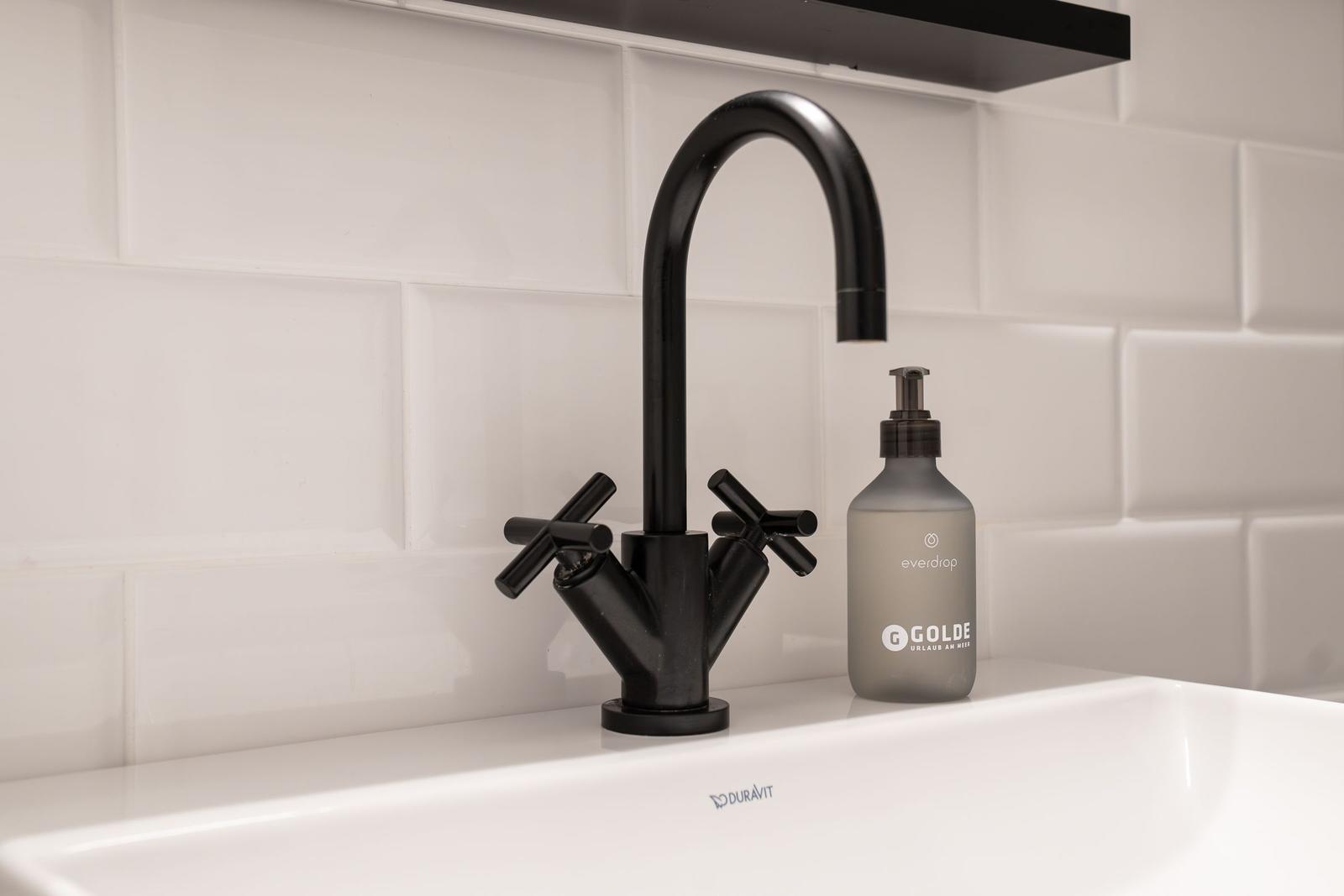 Schwarzer Wasserhahn auf weißem Waschbecken mit Seifenspender.