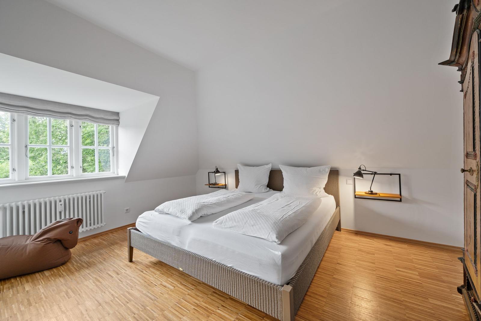 Schlafzimmer mit Doppelbett, Holzboden und Dachfenster mit Blick auf Bäume.