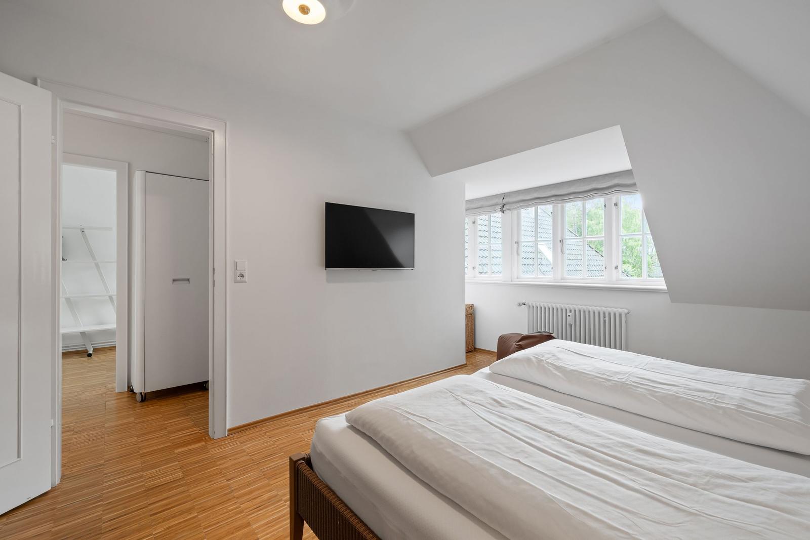 Doppelbettzimmer mit TV, Fenster und Holzboden. Tür führt in einen Flur.