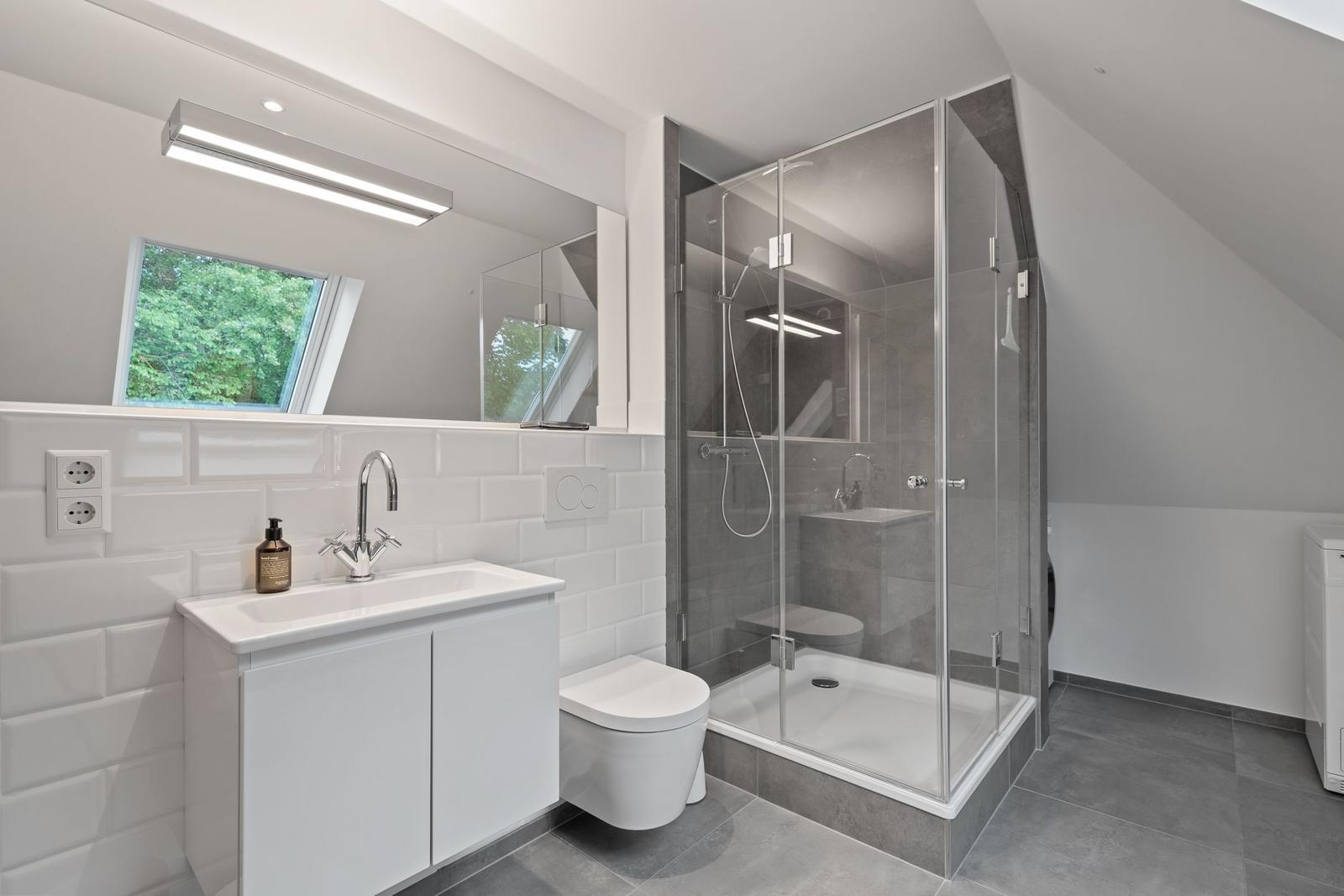 Badezimmer mit Dusche, Waschbecken und Toilette. Fenster mit Blick auf Grün.