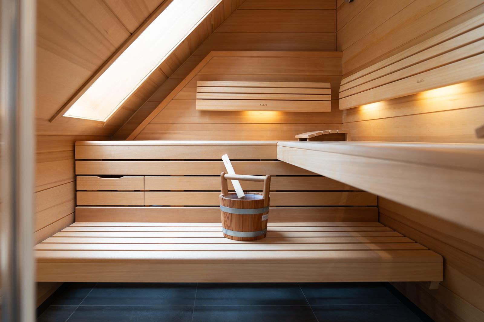Sauna mit Holzbank, Holzwanne und Dachfenster. Fliesenboden und Holzwände.