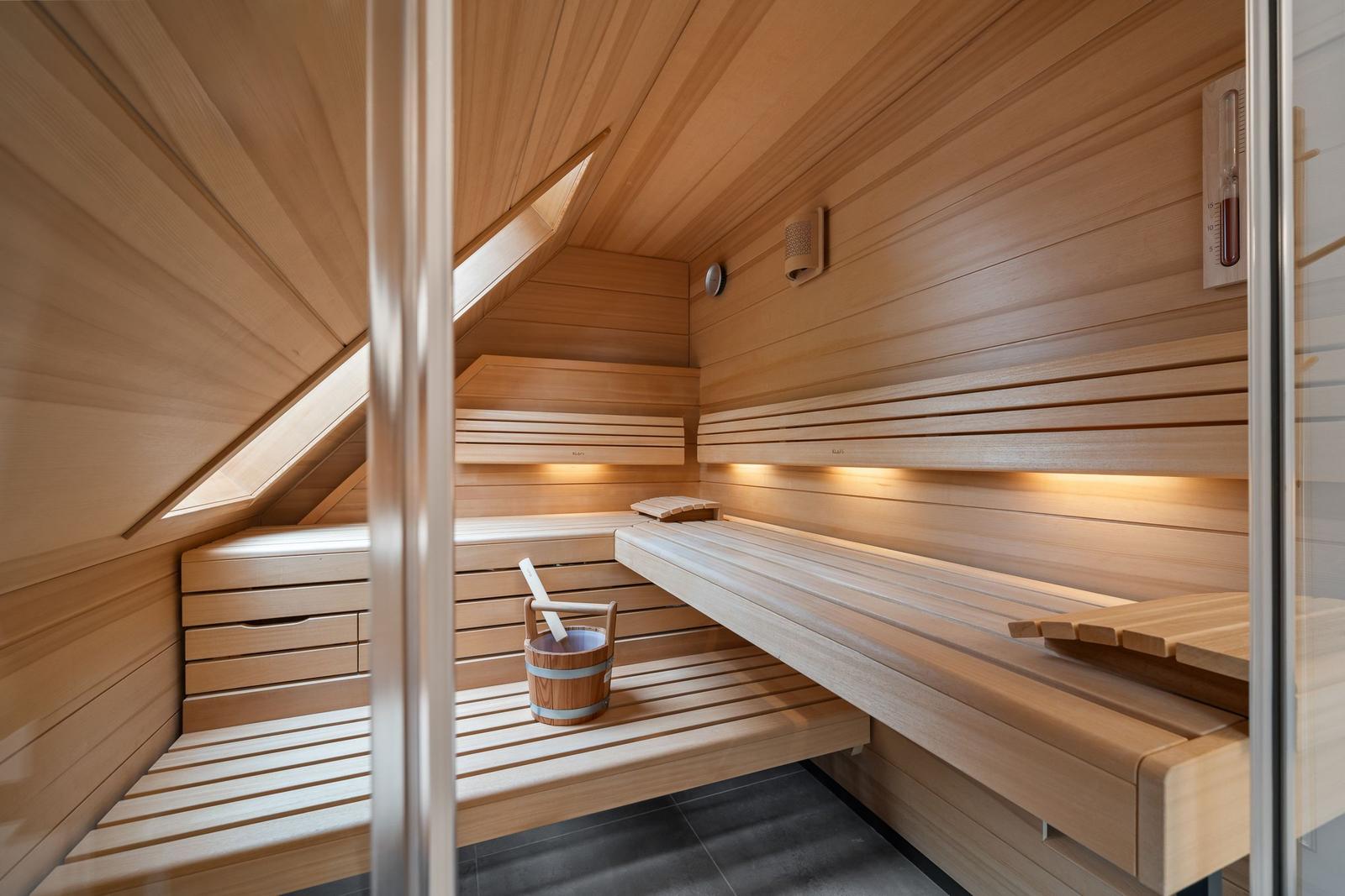 Holzsauna mit mehreren Sitzbänken, Thermometer und Eimer mit Löffel.