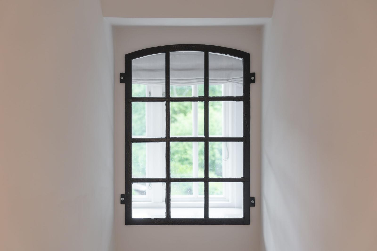 Schwarzes Fenster mit Bogen oben, Blick auf grüne Bäume draußen.