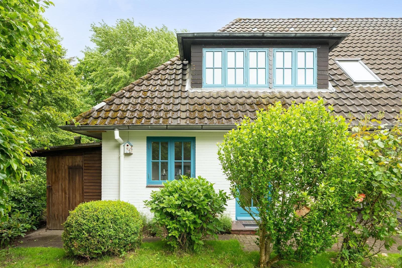 Haus mit weißer Fassade, blauen Fenstern und grüner Umgebung.