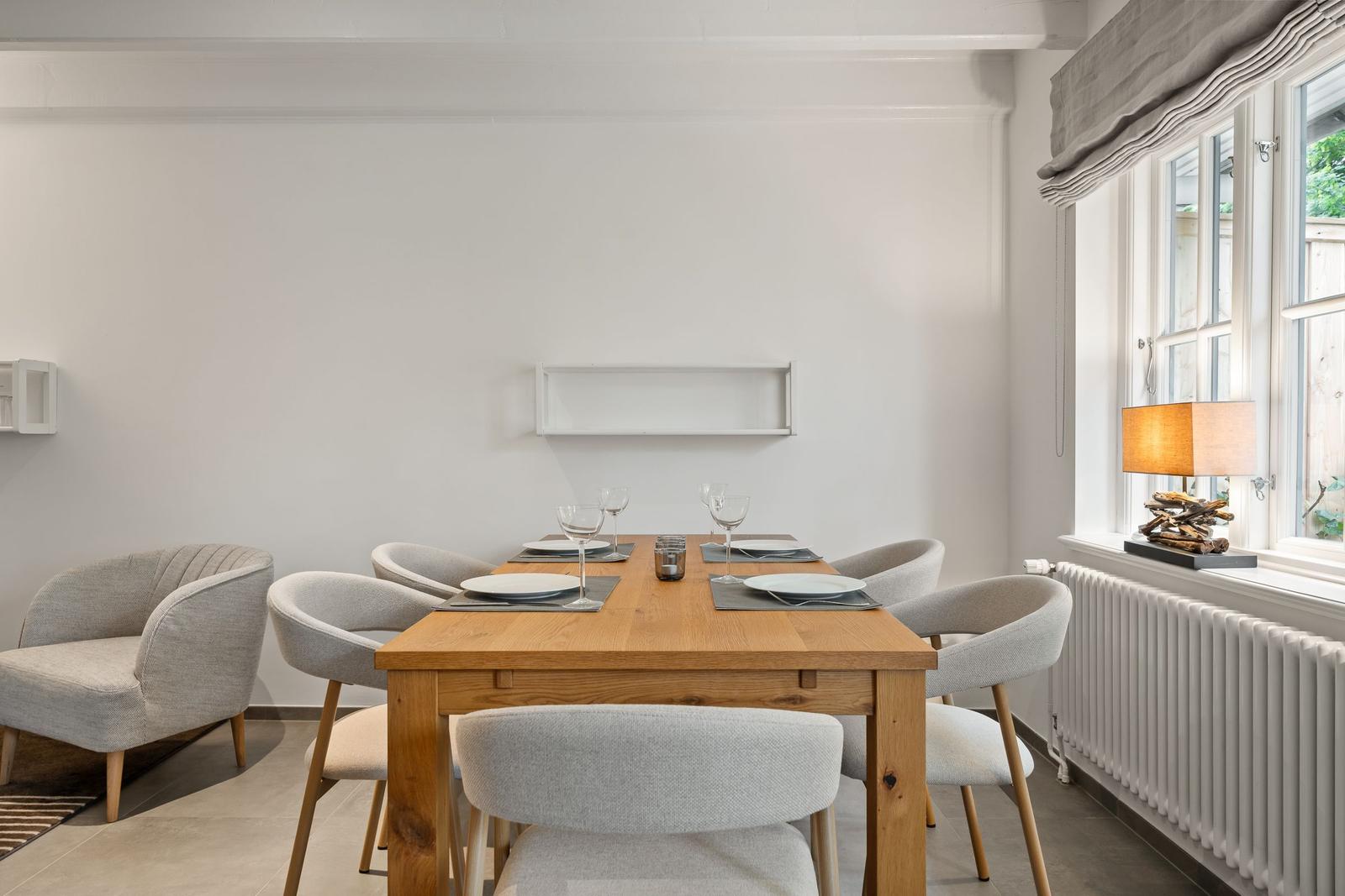 Esszimmer mit Holztisch, grauen Stühlen und Fenster mit Lampe.