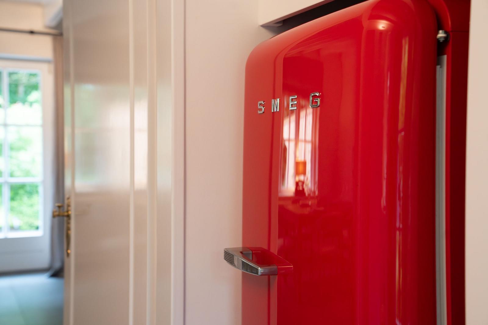 Roter Kühlschrank mit Chromgriff und Markenlogo an der Wand