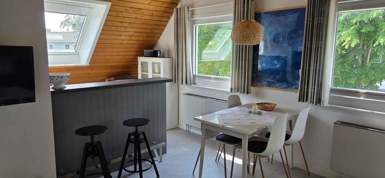 Essbereich mit Tisch, Stühlen und Fenstern. Bar mit Hocker und Fernseher. Holzwand im Dachbereich.