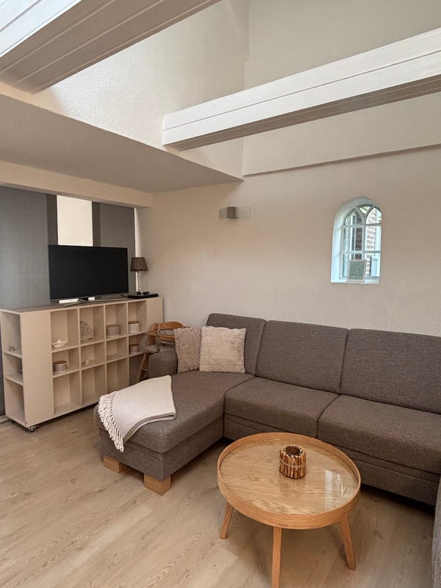 Wohnzimmer mit Ecksofa, runden Tisch und Fernseher an Wand.