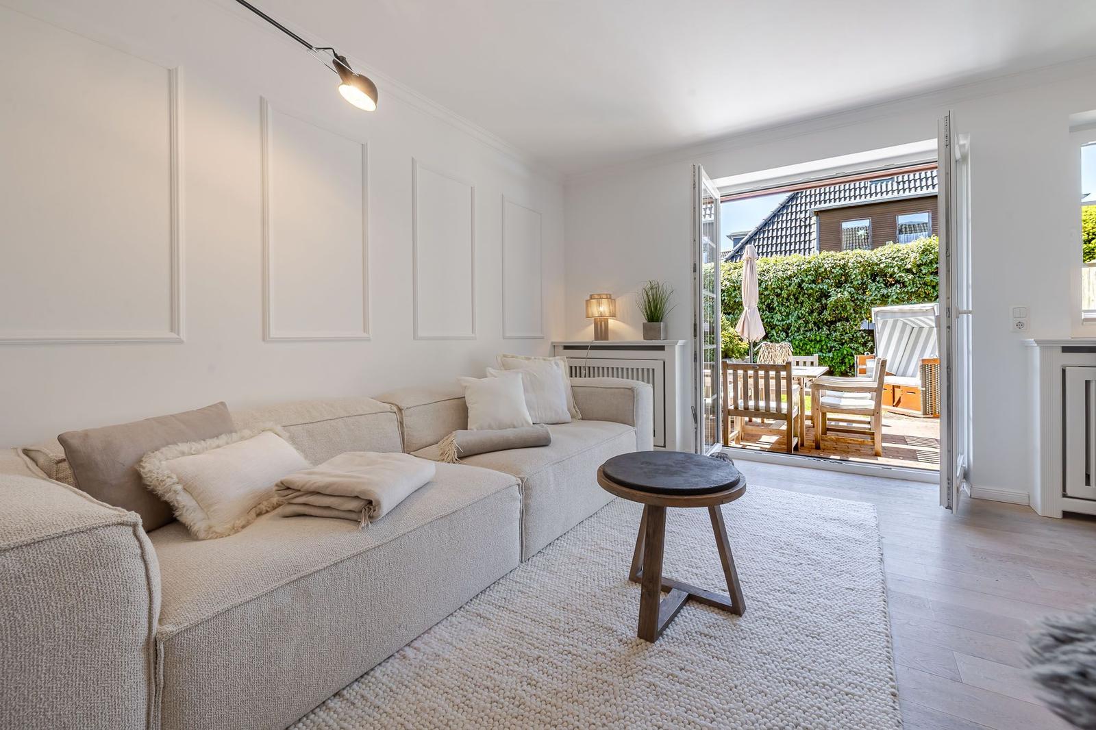 Wohnzimmer mit Sofa, Teppich und Tisch. Durchgehendes Fenster zur Terrasse.
