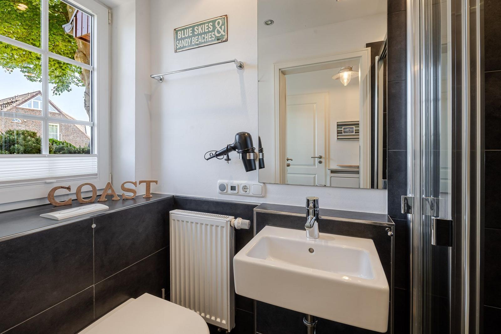 Badezimmer mit Waschbecken, Dusche und Fenster. Wand mit BLUE SKIES SANDY BEACHES Schild.
