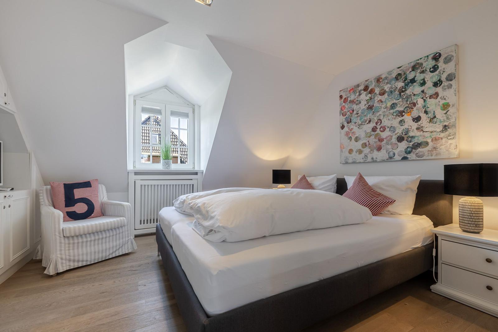 Schlafzimmer mit Bett, Nachttisch und Sessel. An der Wand hängt ein Gemälde.