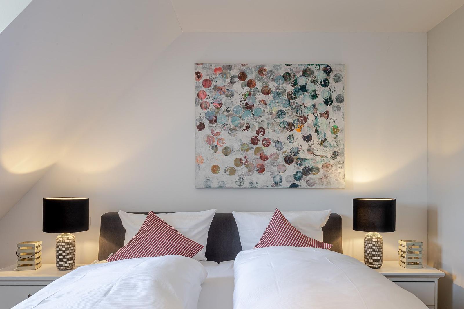 Schlafzimmer mit Doppelbett, Wandbild und Nachttischen mit Lampen.