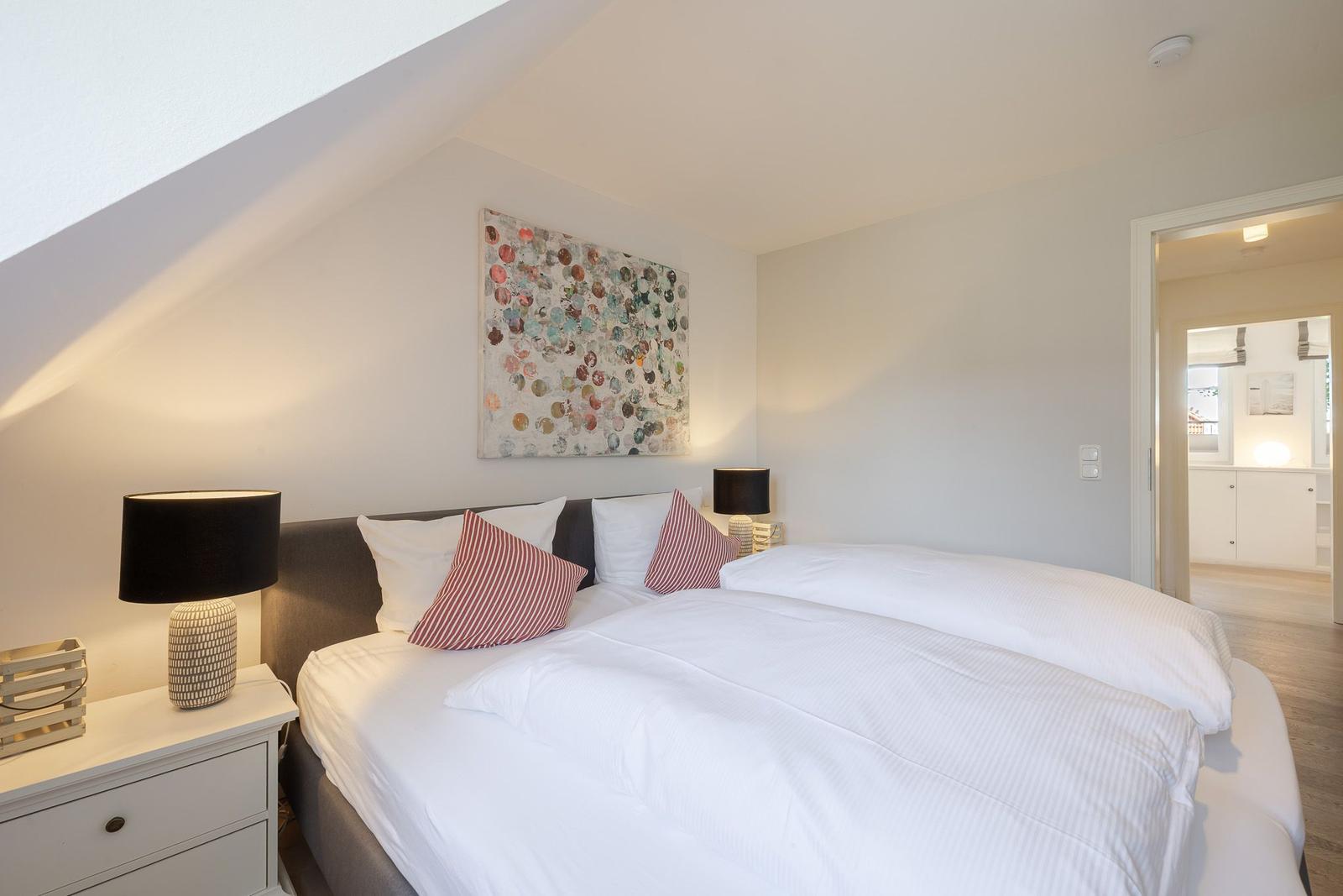Schlafzimmer mit Doppelbett, Nachttischen und Wandbild unter schrägem Dach.