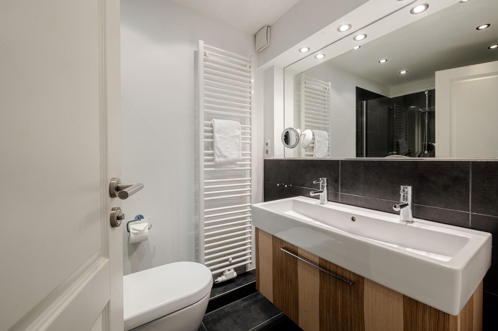 Badezimmer mit Waschbecken, Spiegel, Toilette und Heizkörper.